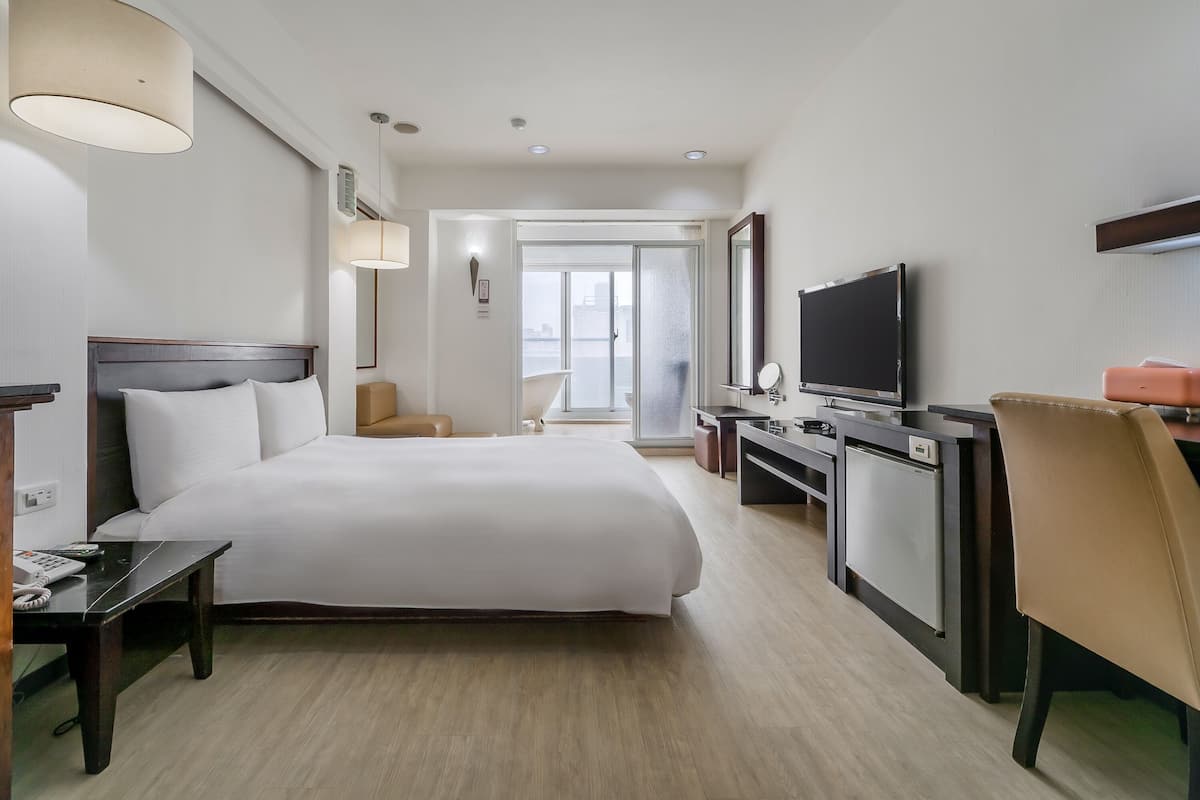 Habitación de hotel con cama, escritorio, silla, televisión y vistas a la ciudad.