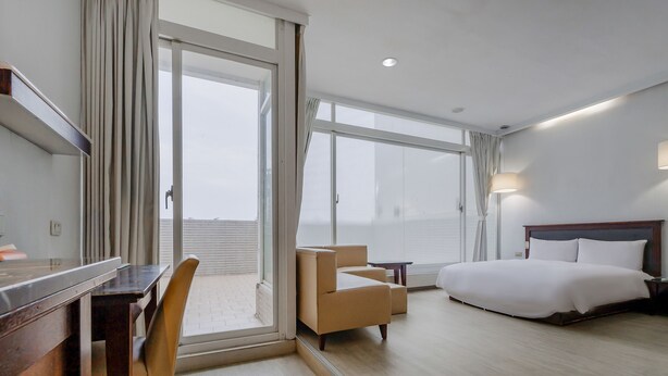 A hotel room with a bed, a desk, a chair, and a view through a large window. - Guide Hotel - Kaohsiung Shinkuchan (Kaohsiung)