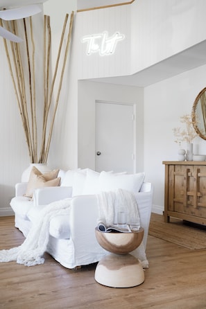 Un dormitorio moderno con un sofá blanco, una mesita de madera y un espejo grande.