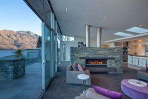 A modern living room with a stone fireplace, comfortable seating, and a view of mountains. - Villa Matau | Gas Fire, Lake Views, A/C, BBQ (Queenstown)