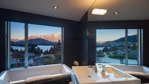 A modern bathroom with two large tubs, a large window offering a mountain view, and a dark interior. - Villa Matau | Gas Fire, Lake Views, A/C, BBQ (Queenstown)