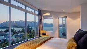 A bedroom with a large window, a bed, a chair, and an air conditioning unit. - Villa Matau | Gas Fire, Lake Views, A/C, BBQ (Queenstown)