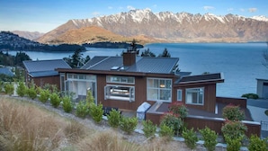 A modern house with a large window overlooking a lake and mountains. - Villa Matau | Gas Fire, Lake Views, A/C, BBQ (Queenstown)