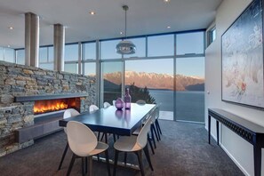 Un espace de repas moderne avec une cheminée en pierre, de grandes fenêtres offrant une vue sur les montagnes et une table à manger avec des chaises.