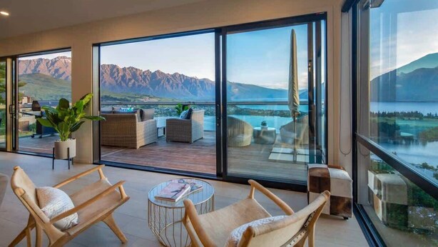A spacious balcony with a view of mountains and a lake, furnished with chairs and a small table. - Highlands Lodge – 5BR Luxury, Lake Views & BBQ (Queenstown)