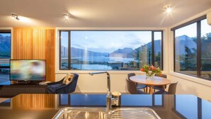 A modern kitchen with a large window, a dining area, and a television. - Highlands Lodge – 5BR Luxury, Lake Views & BBQ (Queenstown)