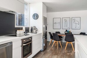 Une cuisine moderne équipée d’un four encastré, d’une machine à café et d’un coin repas avec une table et des chaises.