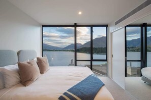 Quarto com cama grande, vista para um lago e montanhas, e porta de correr para área externa.