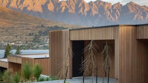 A modern building with a wooden facade, a door, and a view of mountains and a lake. - Lakehouse 2 – Parking, Fireplace, AC, Lake Views (Queenstown)