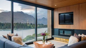 A modern living room with a large window, a flat-screen TV, and a fireplace. - Lakehouse 2 – Parking, Fireplace, AC, Lake Views (Queenstown)