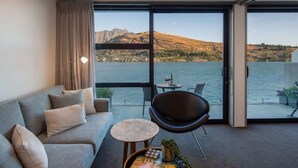A modern room with a sofa, a chair, a small table, and a view of a lake and mountains. - Kikorangi | Lake View, BBQ, A/C & Free Parking (Queenstown)