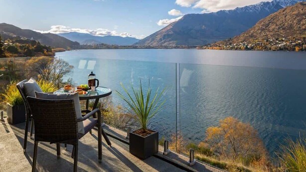 A terrace with a table and chairs overlooking a lake with mountains in the background. - Kikorangi | Lake View, BBQ, A/C & Free Parking (Queenstown)