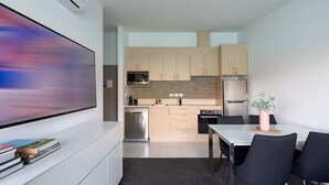 A modern kitchen with a dining area, a flat-screen TV, and a large painting on the wall. - Kikorangi | Lake View, BBQ, A/C & Free Parking (Queenstown)