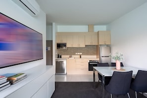 A modern kitchen with a dining area, a flat-screen TV, and a large painting on the wall.