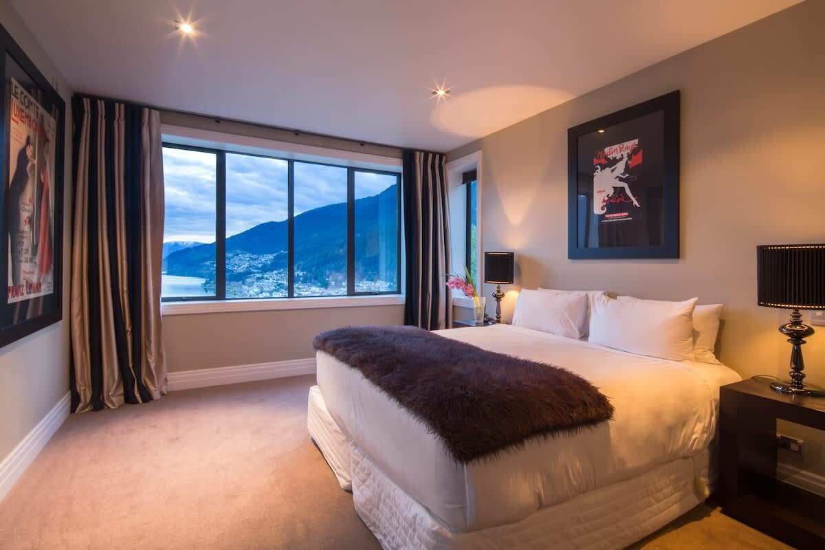 A bedroom with a large window, a bed, a nightstand, and a framed picture on the wall.