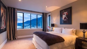 Un dormitorio con un ventanal grande, una cama, una mesita de noche y un cuadro enmarcado en la pared.