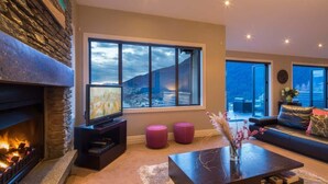 Una sala de estar moderna con chimenea, un ventanal con vistas a la montaña, un televisor de pantalla plana y un sofá.