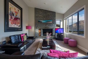 Un salon moderne avec une cheminée en pierre, un grand téléviseur et une vue sur les montagnes.