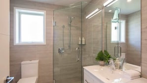 A modern bathroom with a glass-enclosed shower, a toilet, a sink with a mirror, and a window providing natural light. - Hillside Villa 4 – Modern 2BR Walk to Town & A/C (Queenstown)