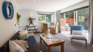 A spacious living area with a sofa, a coffee table, and a dining table with chairs. There is a large window providing a view of the outdoors. - Hillside Villa 4 – Modern 2BR Walk to Town & A/C (Queenstown)