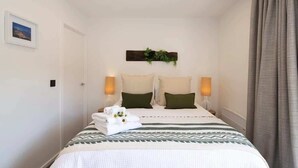 A hotel room with a bed, two bedside lamps, a wall-mounted plant, and a framed picture. - Hillside Villa 4 – Modern 2BR Walk to Town & A/C (Queenstown)