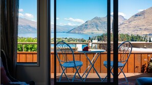 Enjoy breathtaking views of the surrounding mountains and water from this room's balcony, featuring a comfortable seating area with a table and a beautiful flower.