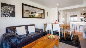Uma sala de estar moderna com um sofá de couro, uma mesa de centro de madeira e um espaço de refeições com cadeiras brancas.