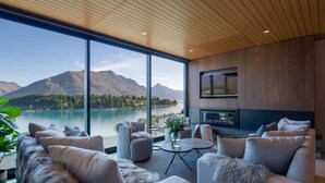 A modern living room with a large window overlooking a lake and mountains, furnished with sofas and a coffee table. - Lakehouse 4 – Parking, Fireplace, Lake Views (Queenstown)
