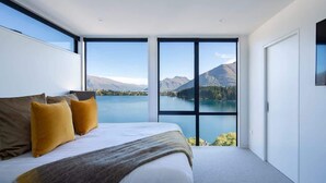 A bedroom with a large bed, two windows, and a view of a lake and mountains. - Lakehouse 4 – Parking, Fireplace, Lake Views (Queenstown)