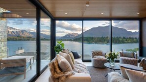 A modern living room with a large window overlooking a lake and mountains. - Lakehouse 4 – Parking, Fireplace, Lake Views (Queenstown)