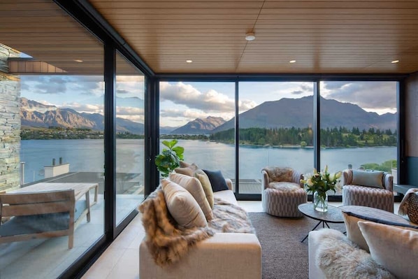 Un salon moderne doté d’une grande fenêtre donnant sur un lac et des montagnes.