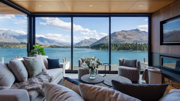 A modern living room with a large window overlooking a lake and mountains. - Lakehouse 4 – Parking, Fireplace, Lake Views (Queenstown)