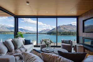 Un salon moderne doté d’une grande fenêtre donnant sur un lac et des montagnes.