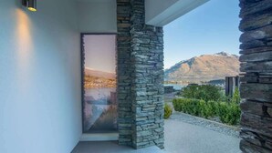 A modern exterior with a stone column, a glass door, and a view of mountains. - Aurora Lodge– Hot Tub, Fireplace & Lake Views, BBQ (Queenstown)