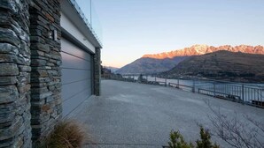 A stone building with a flat roof, a paved area, and a view of mountains and a body of water. - Aurora Lodge– Hot Tub, Fireplace & Lake Views, BBQ (Queenstown)