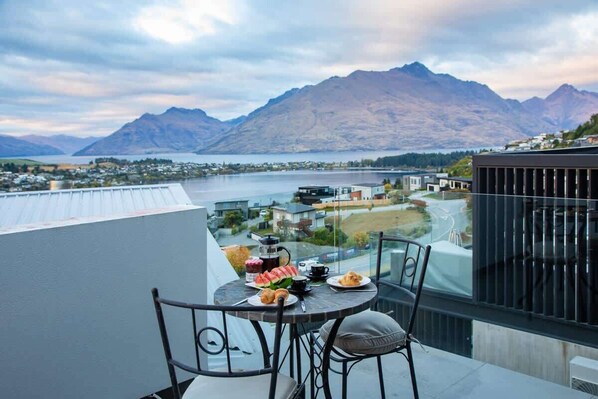 Un balcon avec une table préparée pour le petit-déjeuner, offrant une vue sur un lac et des montagnes.