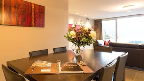A modern dining area with a dark wooden table, a vase of flowers, and a book titled 'ONE @ 25 BELFAST'. - Luxury on Belfast | BBQ, Gas Fire, A/C, Parking (Queenstown)