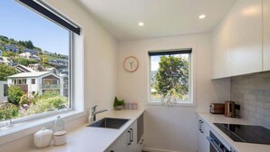 A modern kitchen with white cabinetry, a built-in oven, and a window with a view of houses. - Hillside Villa 3 – Modern 2BR Walk to Town & A/C (Queenstown)