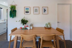 Un coin repas avec une table en bois, quatre chaises, une plante en pot, des tableaux encadrés au mur et une porte à l’arrière-plan.