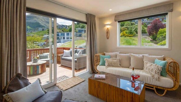 A spacious living room with a sofa, coffee table, and a view of a deck and mountains. - Hillside Villa 3 – Modern 2BR Walk to Town & A/C (Queenstown)