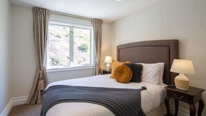Una habitación de hotel con una cama grande, dos mesitas de noche, un ventanal con cortinas y vistas al exterior.