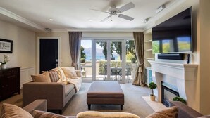Un salón con sofá, reposapiés, televisor de pantalla plana, chimenea y vistas a través de un ventanal.