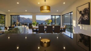 A modern dining area with a large table, chairs, and a view of mountains and a lake. - Highlands House – Lake Views, BBQ & Luxury Stay (Queenstown)