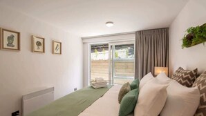 A bedroom with a bed, a radiator, a window with curtains, and framed pictures on the wall. - Hillside Villa 2 – Modern 2BR Walk to Town & A/C (Queenstown)