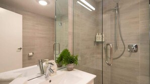 A modern bathroom with a glass-enclosed shower, a white sink, and a potted plant. - Hillside Villa 2 – Modern 2BR Walk to Town & A/C (Queenstown)