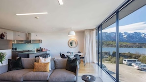 A modern living room with a sofa, dining table, and kitchen area. - Villa Pukaki | Gas Fire, Free Parking, Lake Views (Queenstown)