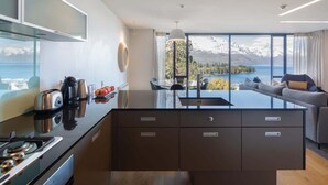 A modern kitchen with a central island, a dining area with a view of a lake and mountains, and a seating area with a sofa and a table. - Villa Pukaki | Gas Fire, Free Parking, Lake Views (Queenstown)