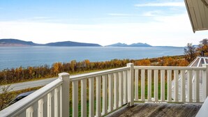 Een houten terras met een witte balustrade, uitkijkend op een waterpartij en verre bergen.