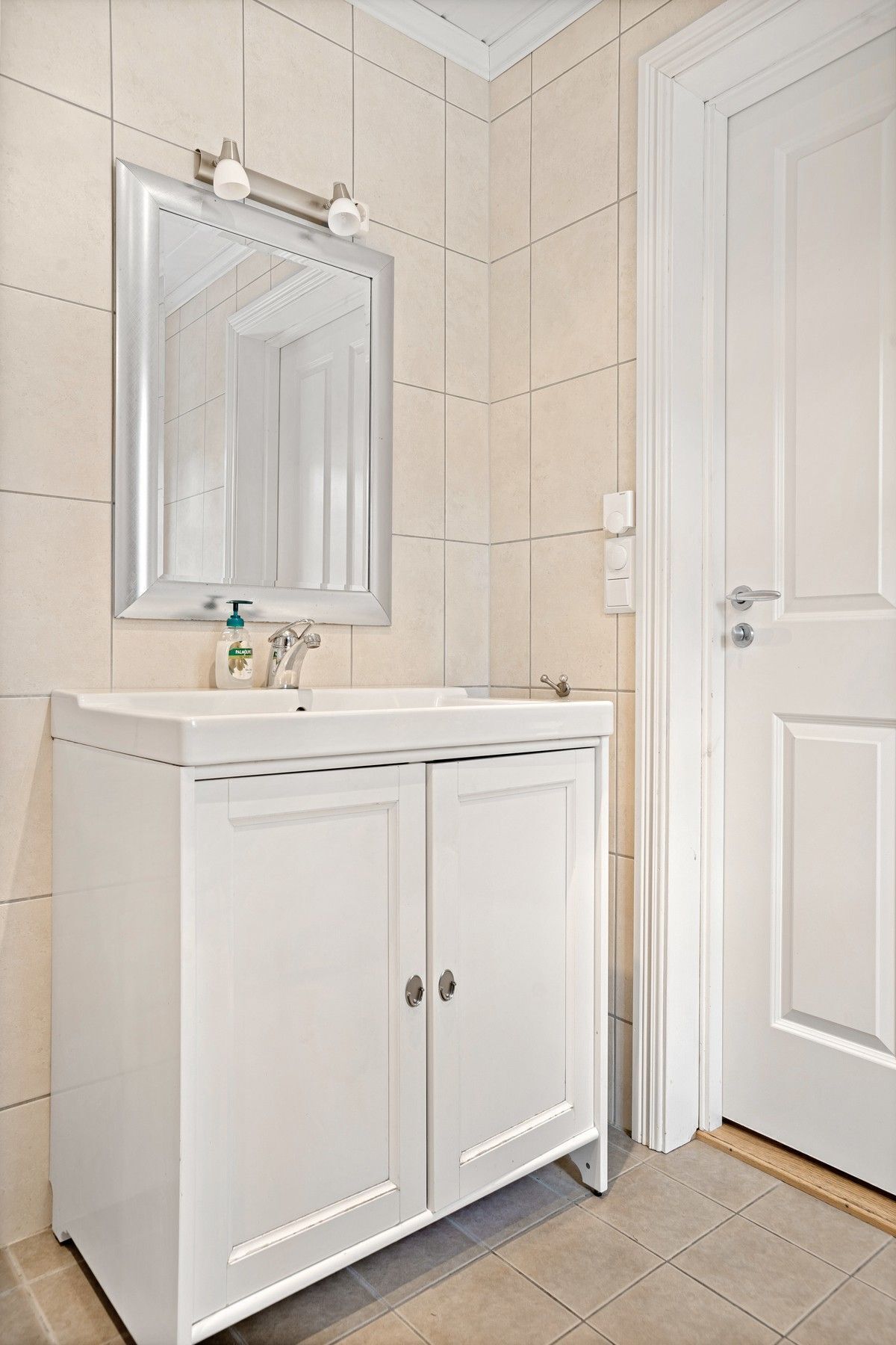 Un baño con tocador blanco, espejo y puerta.