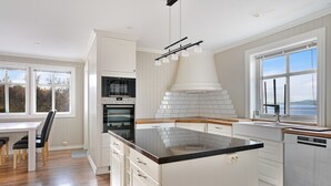 Een keuken met een centraal eiland, witte kastjes, een ingebouwde oven en een groot raam met uitzicht.
